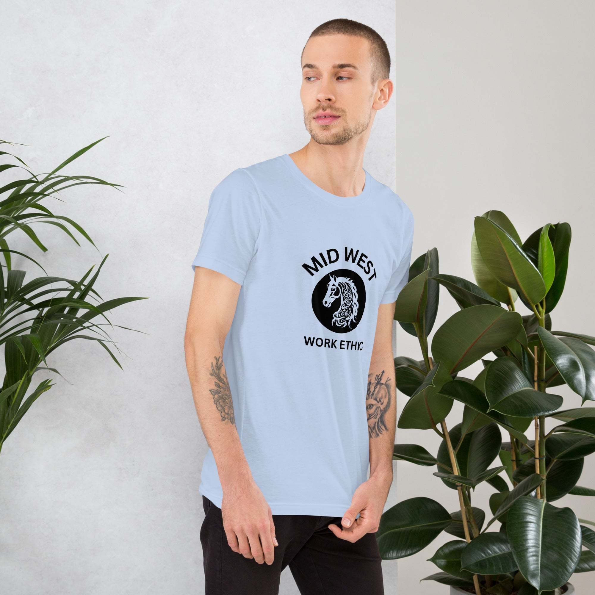 Man wearing light blue Midwest T-Shirt with horse graphic and "Mid West Work Ethic" text, standing near green plants