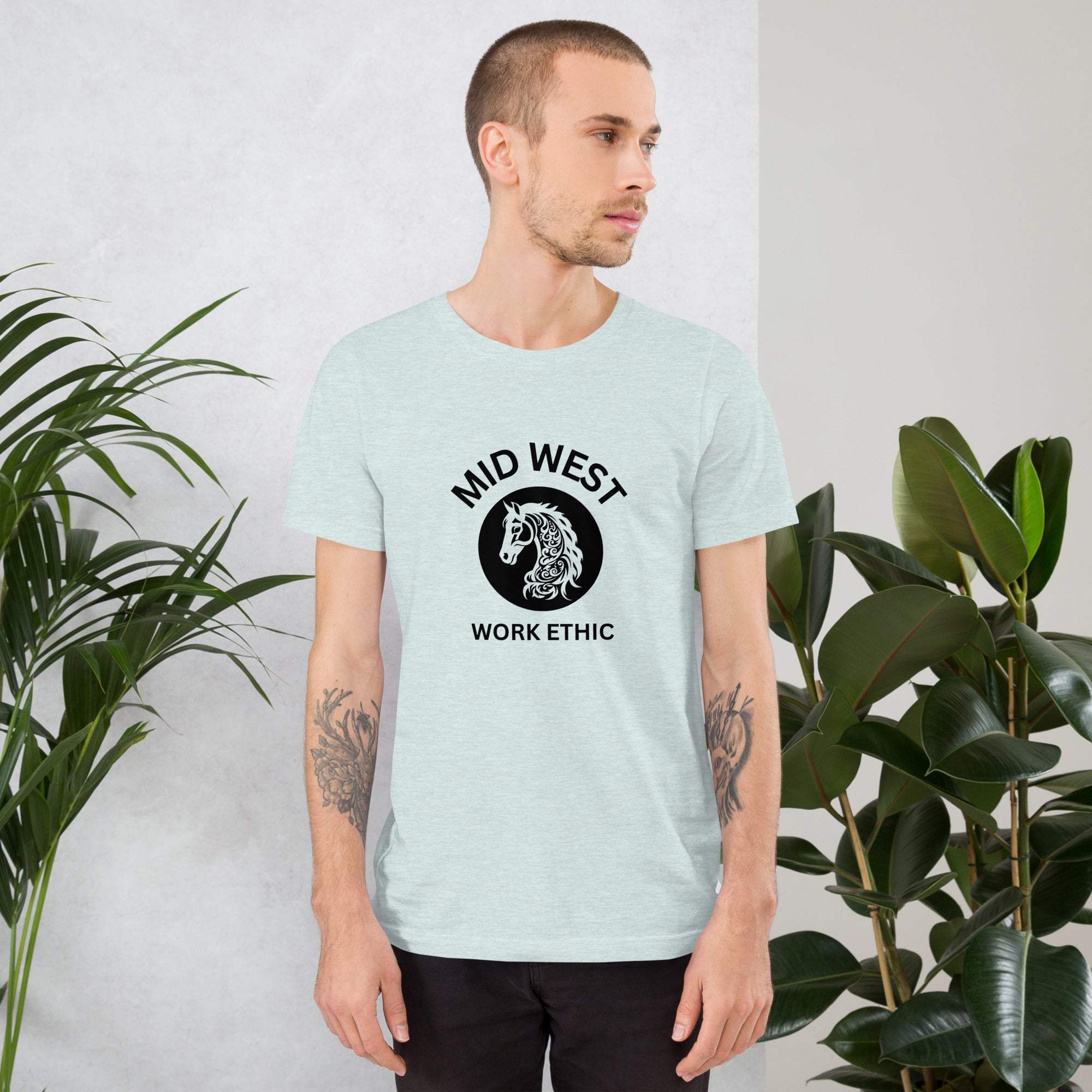 Man wearing Midwest T-Shirt with horse graphic and work ethic text, standing indoors near green plants