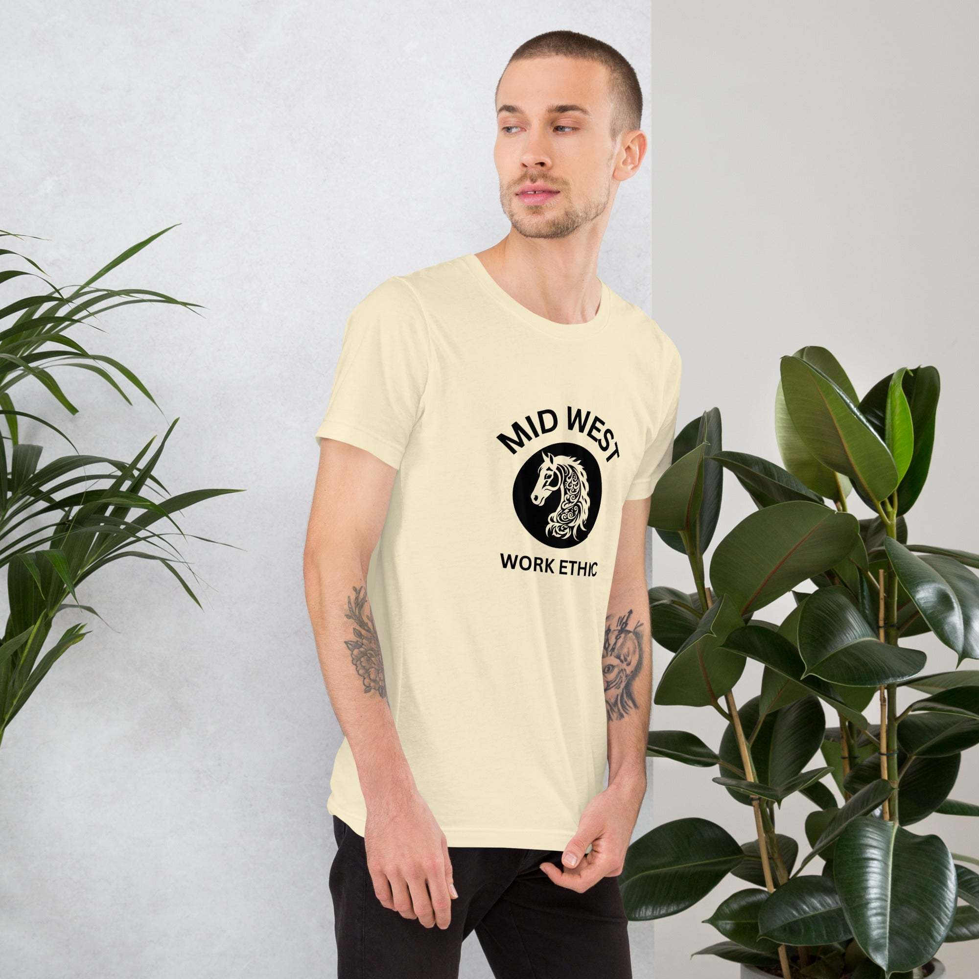 Man wearing Midwest T-Shirt with horse graphic and work ethic text standing near plants