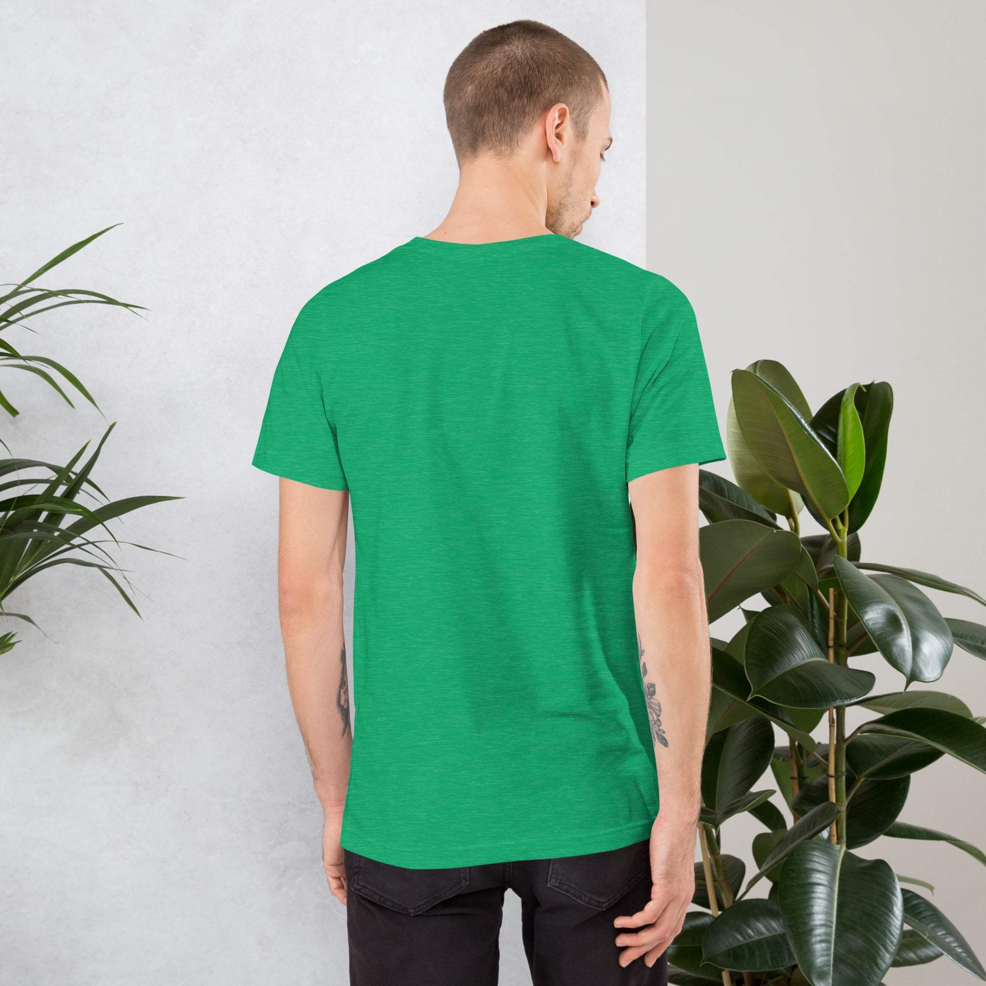 Back view of man wearing plain green vintage aesthetic frog and mushroom t-shirt standing near indoor plants