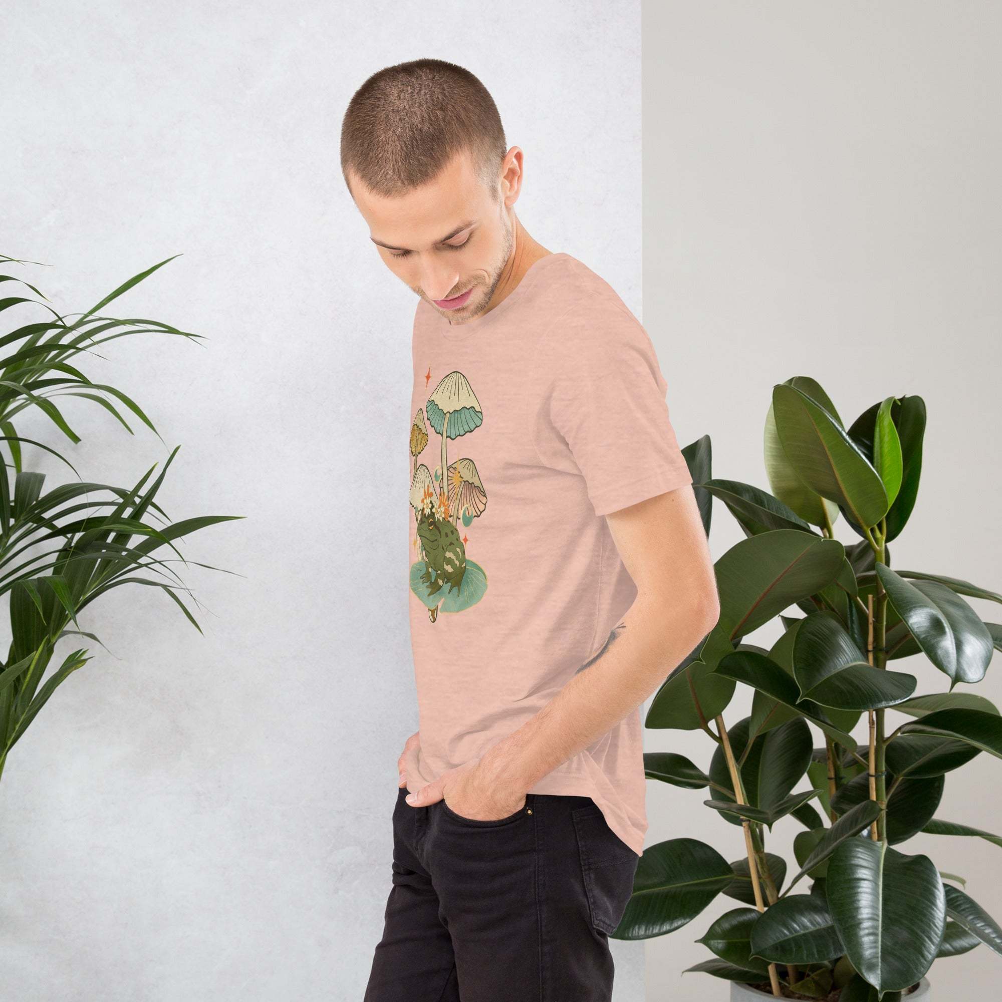 young man wearing vintage aesthetic frog and mushroom t-shirt standing near green plants