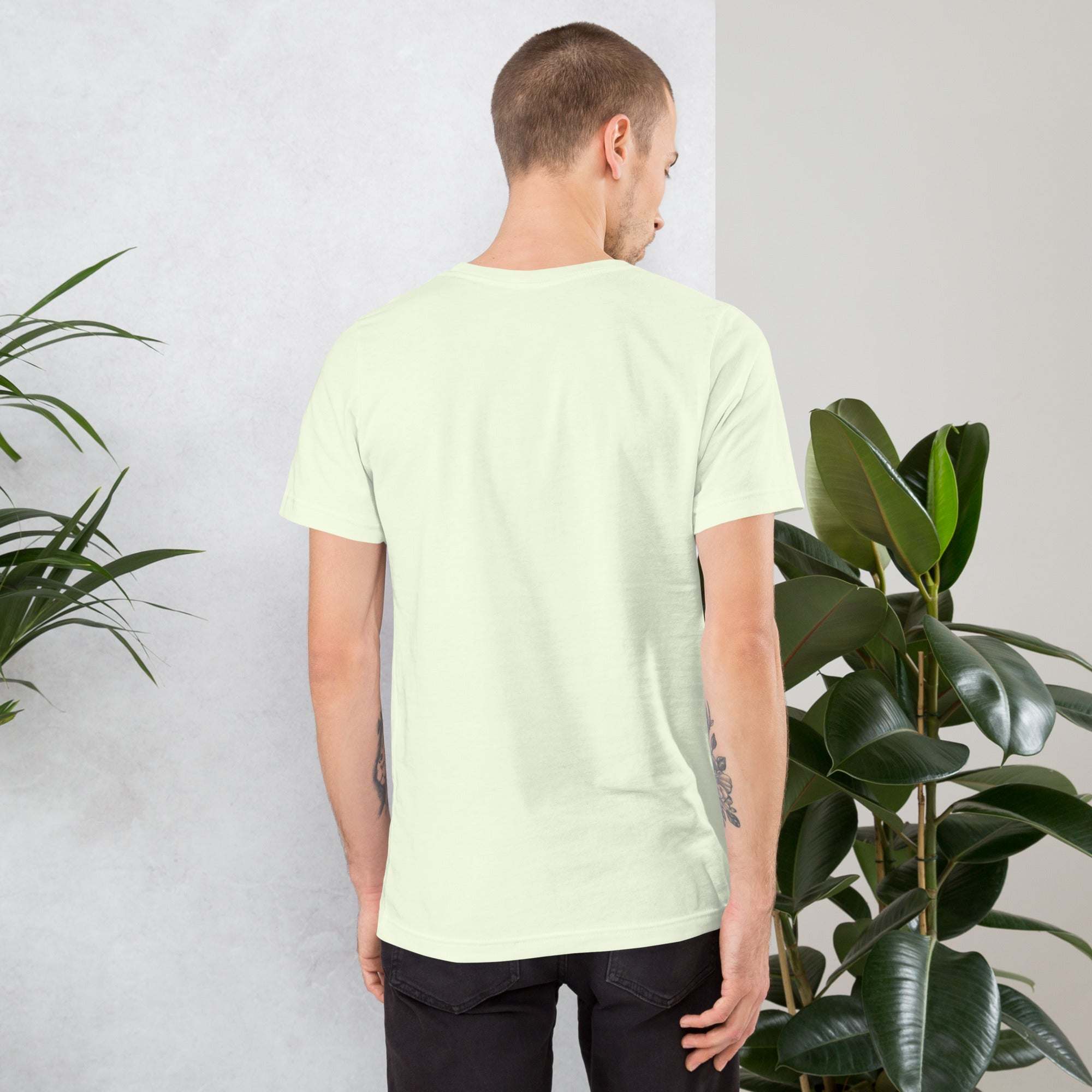 Back view of man wearing plain light green vintage aesthetic frog and mushroom t-shirt surrounded by plants