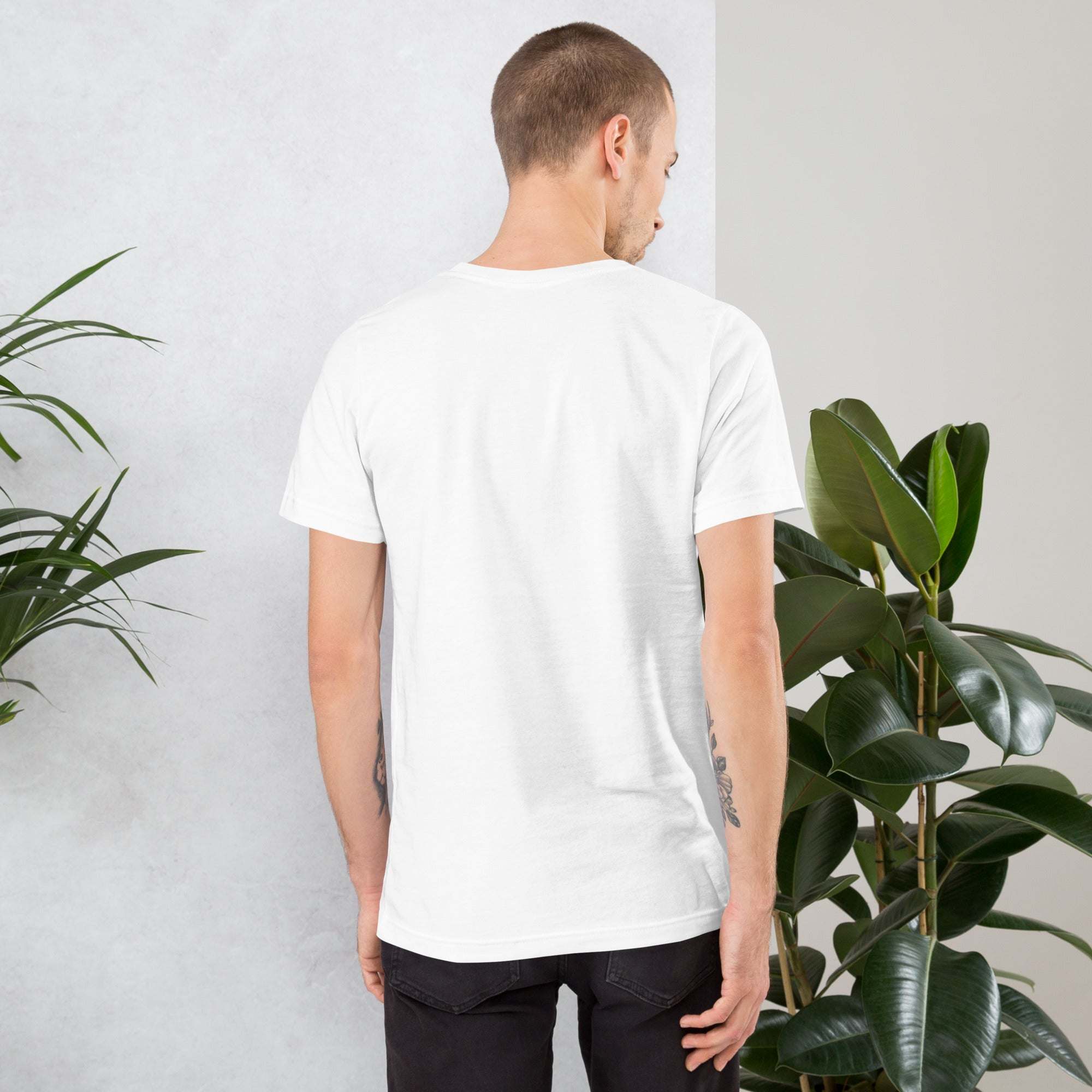 Back view of man wearing plain white Frog and Mushroom T-Shirt standing near green plants