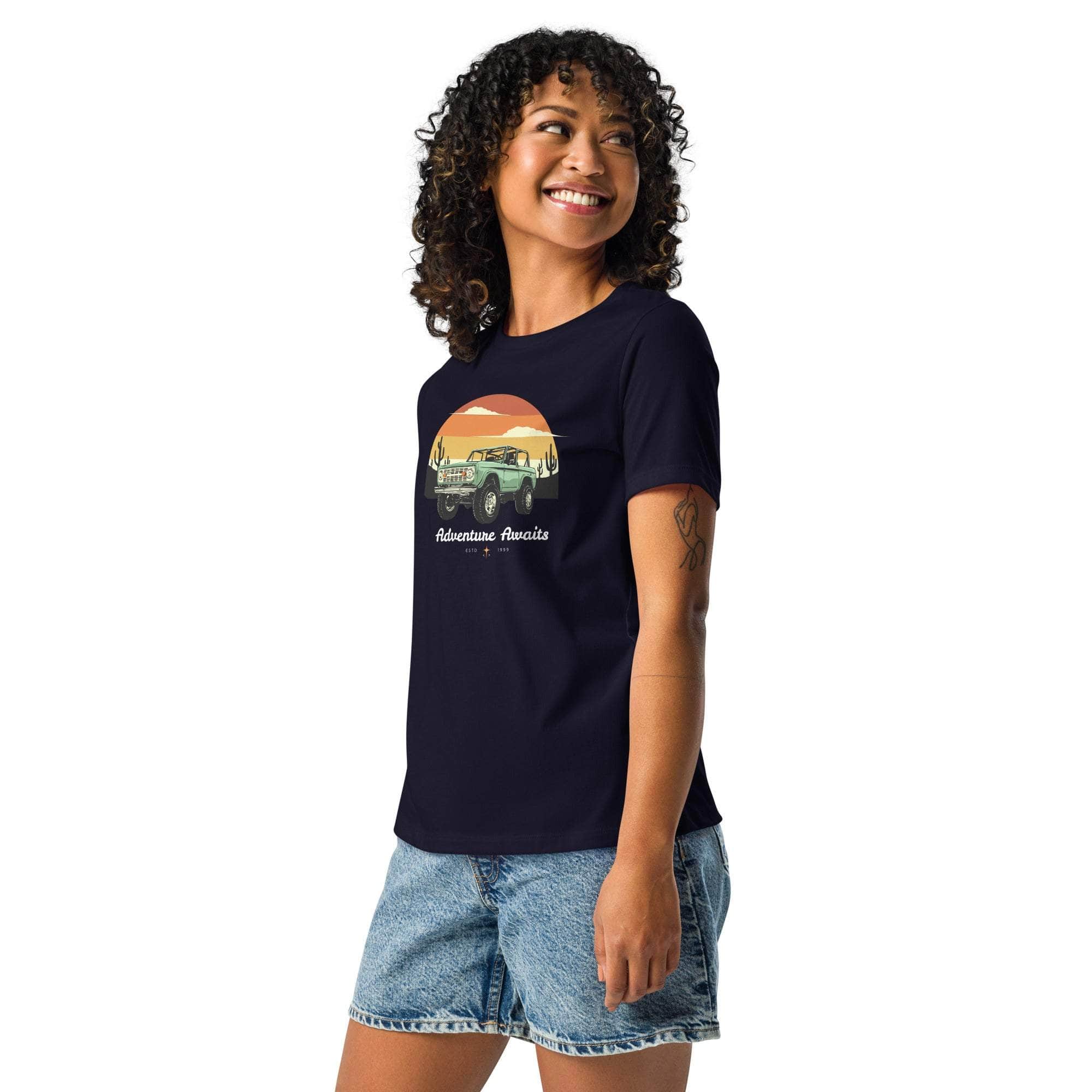 Woman wearing navy Adventure Awaits T-Shirt with off-road vehicle and desert sunset design paired with denim shorts