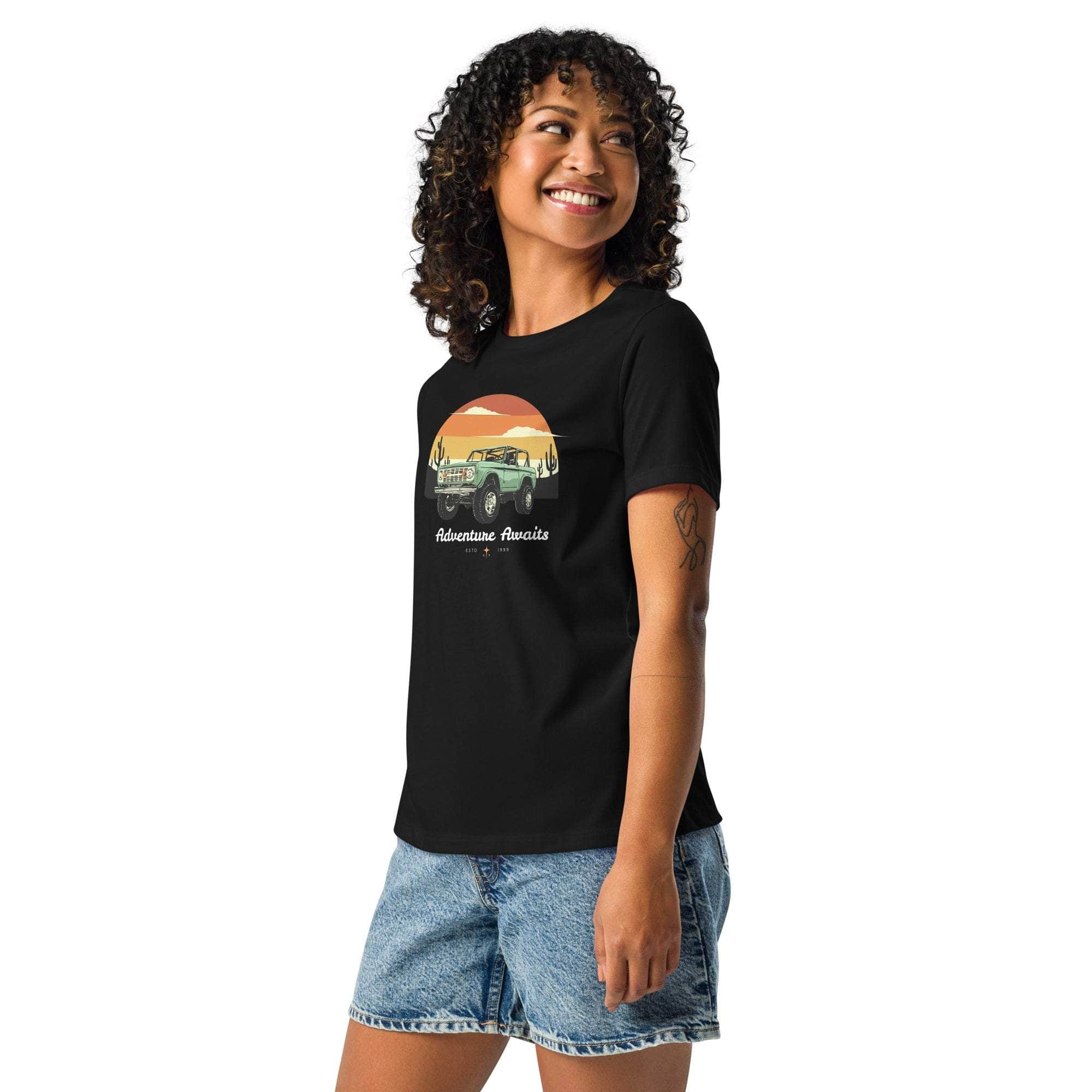 Woman wearing black Adventure Awaits T-Shirt with off-road desert sunset design and denim shorts