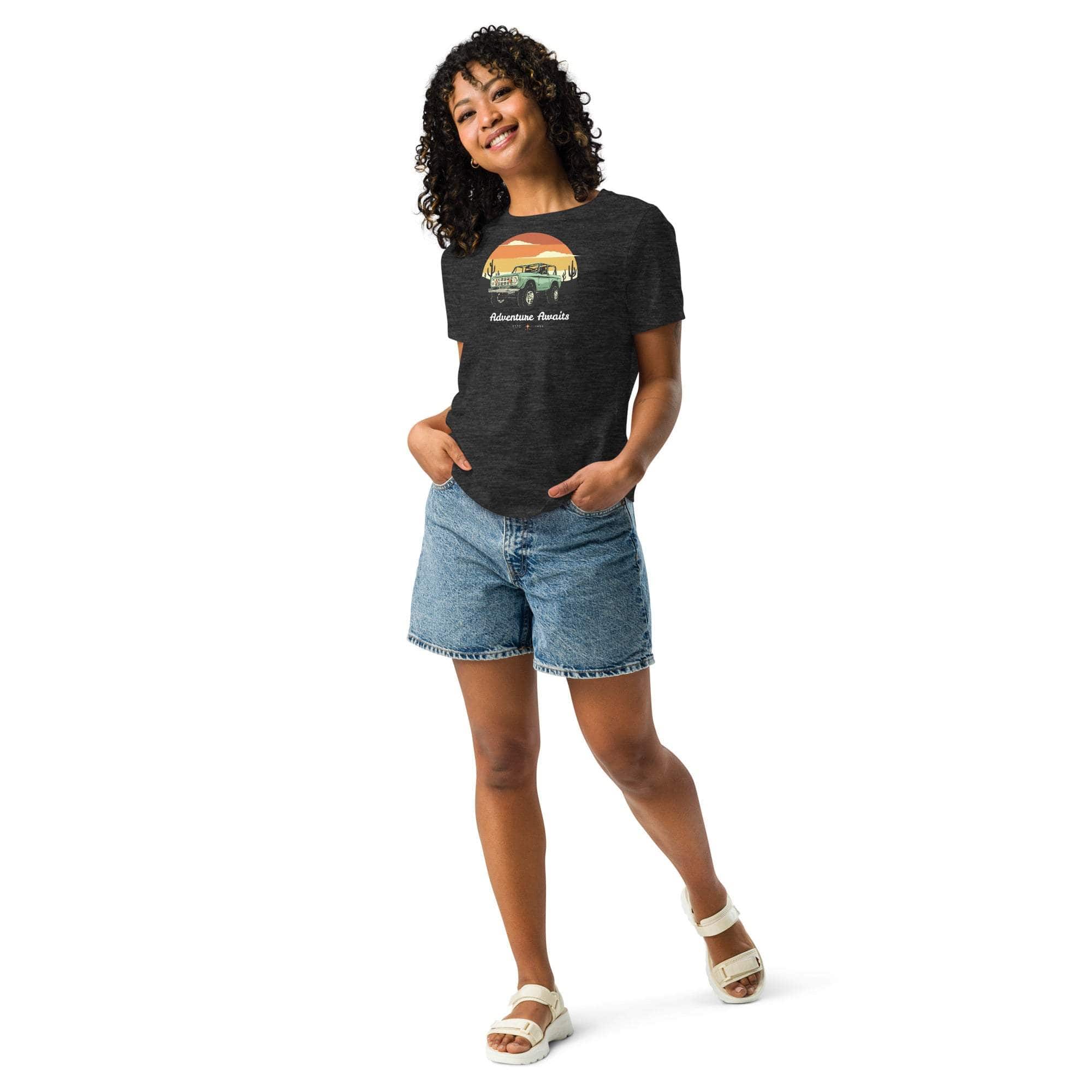 Woman wearing black Adventure Awaits T-Shirt with off-road vehicle and desert sunset design paired with denim shorts