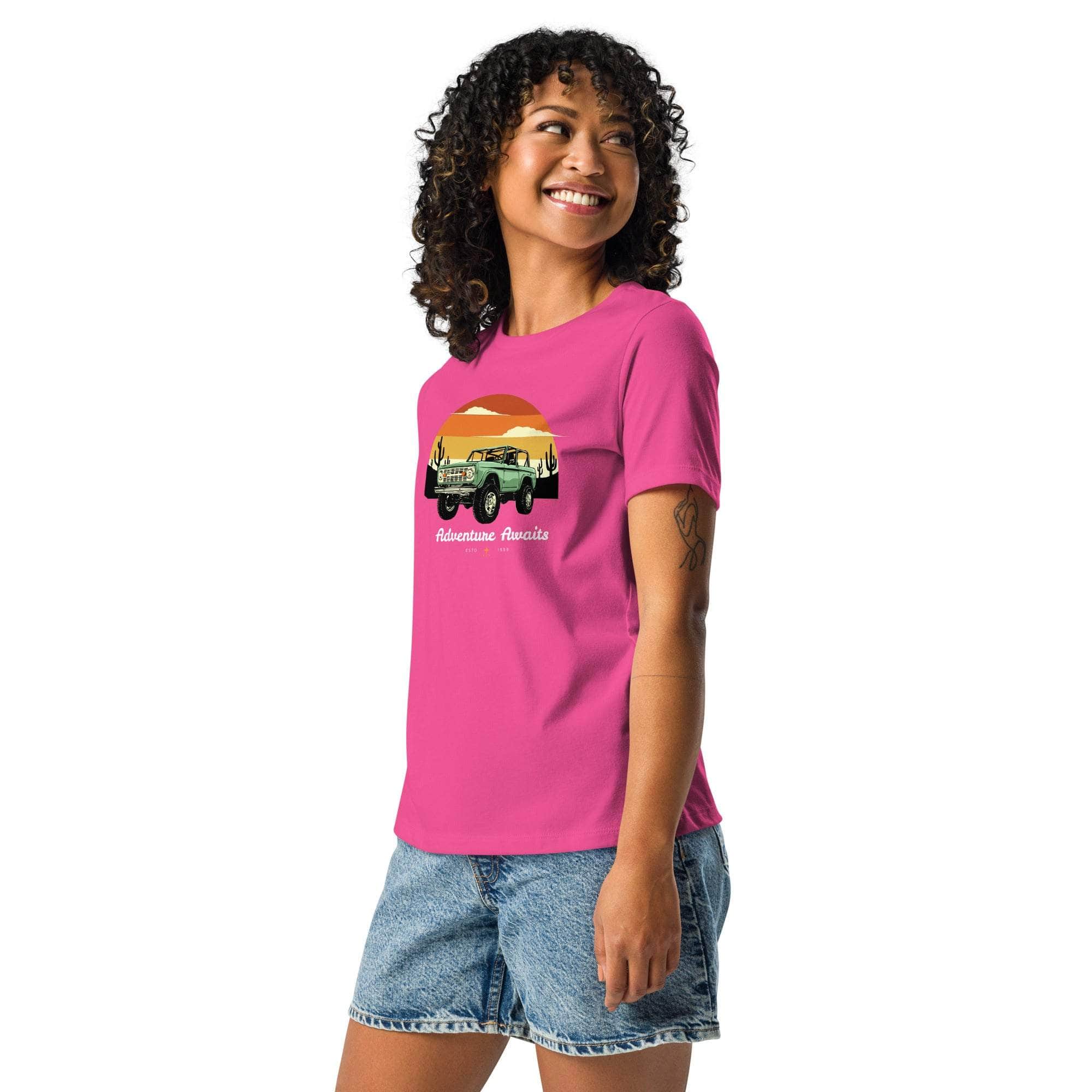Woman wearing pink Adventure Awaits T-Shirt with off-road vehicle and desert sunset design