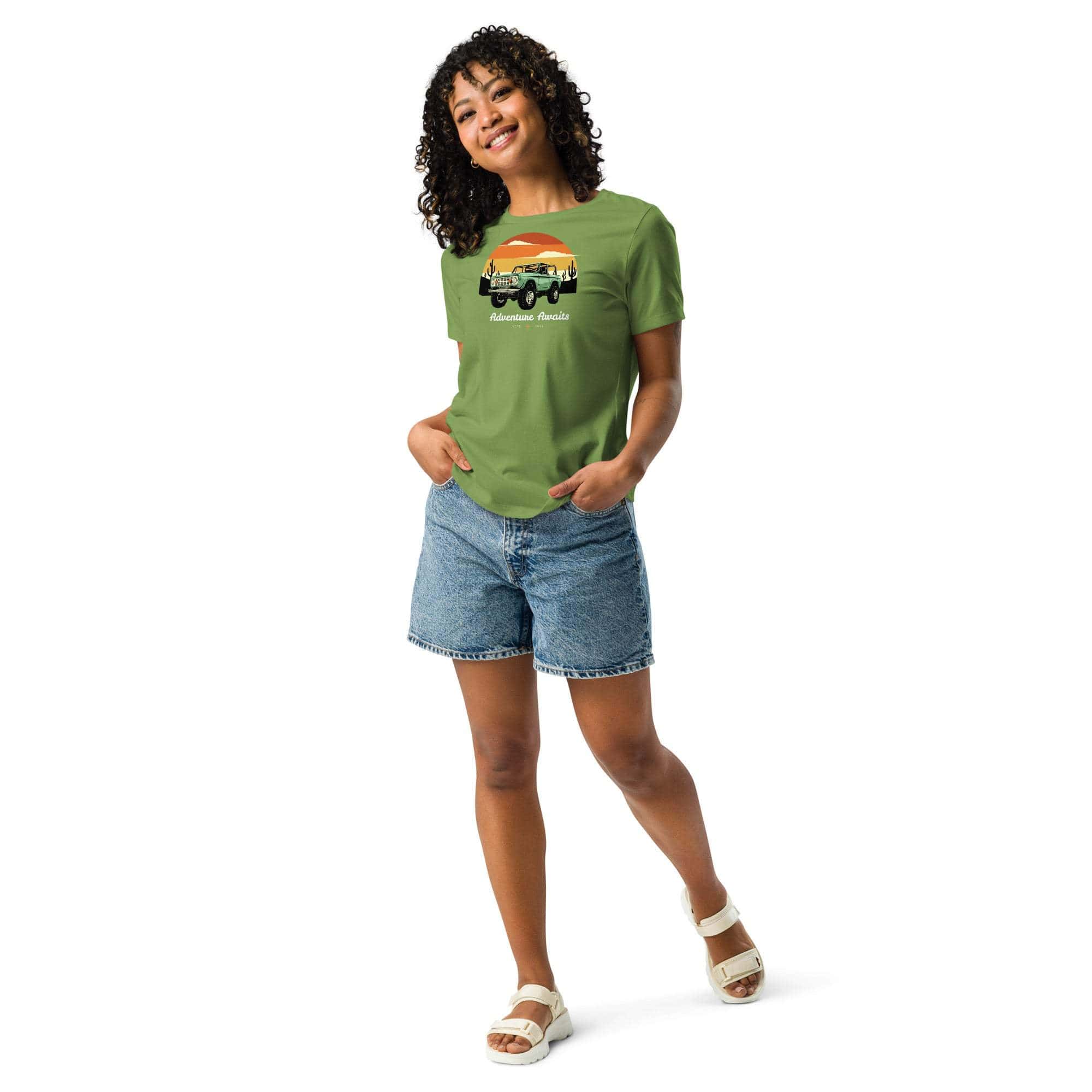 Woman wearing green Adventure Awaits T-Shirt with off-road vehicle and desert sunset design paired with denim shorts