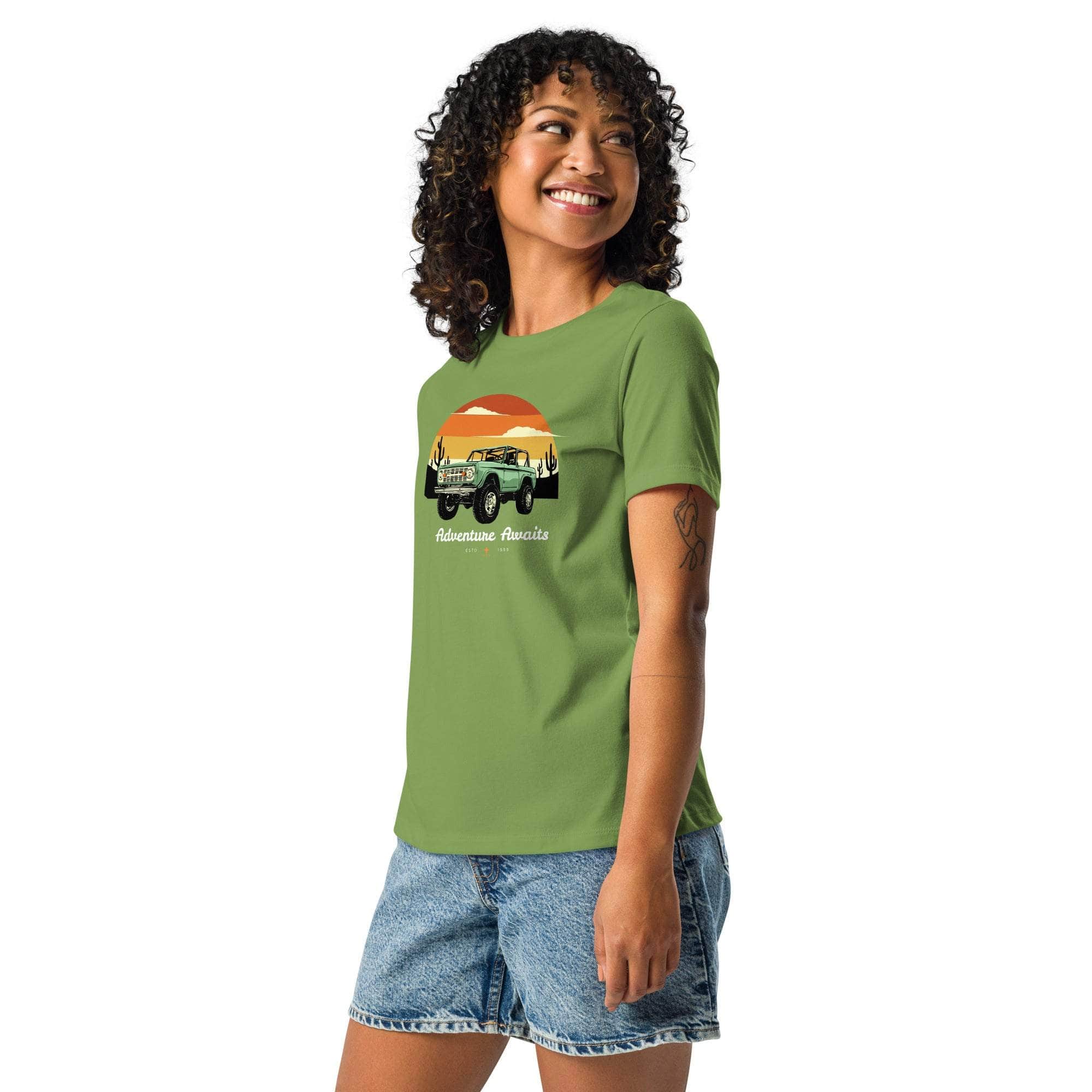 Woman wearing green Adventure Awaits T-Shirt with off-road vehicle and desert sunset design