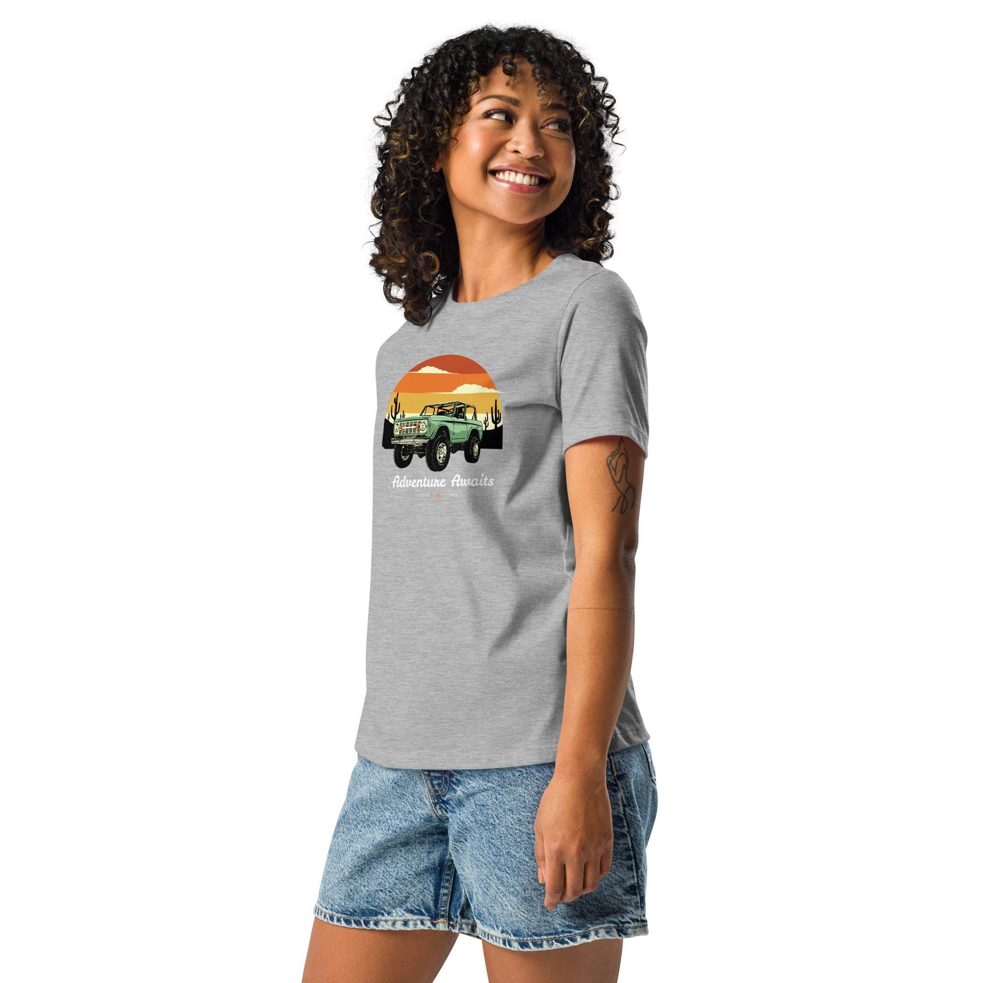 Woman wearing gray Adventure Awaits T-Shirt with off-road vehicle and desert sunset design