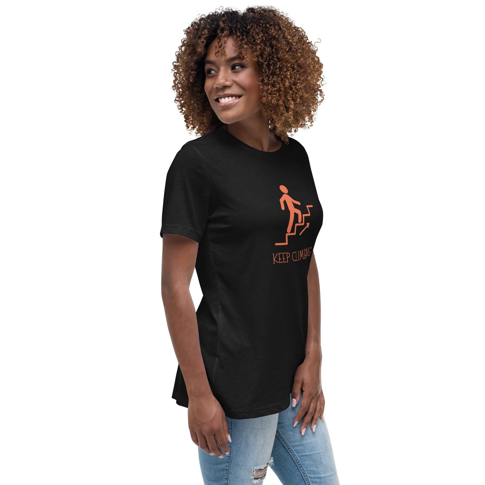 Black Keep Climbing women's t-shirt with orange graphic and motivational text, worn by smiling woman with curly hair, paired with ripped jeans.