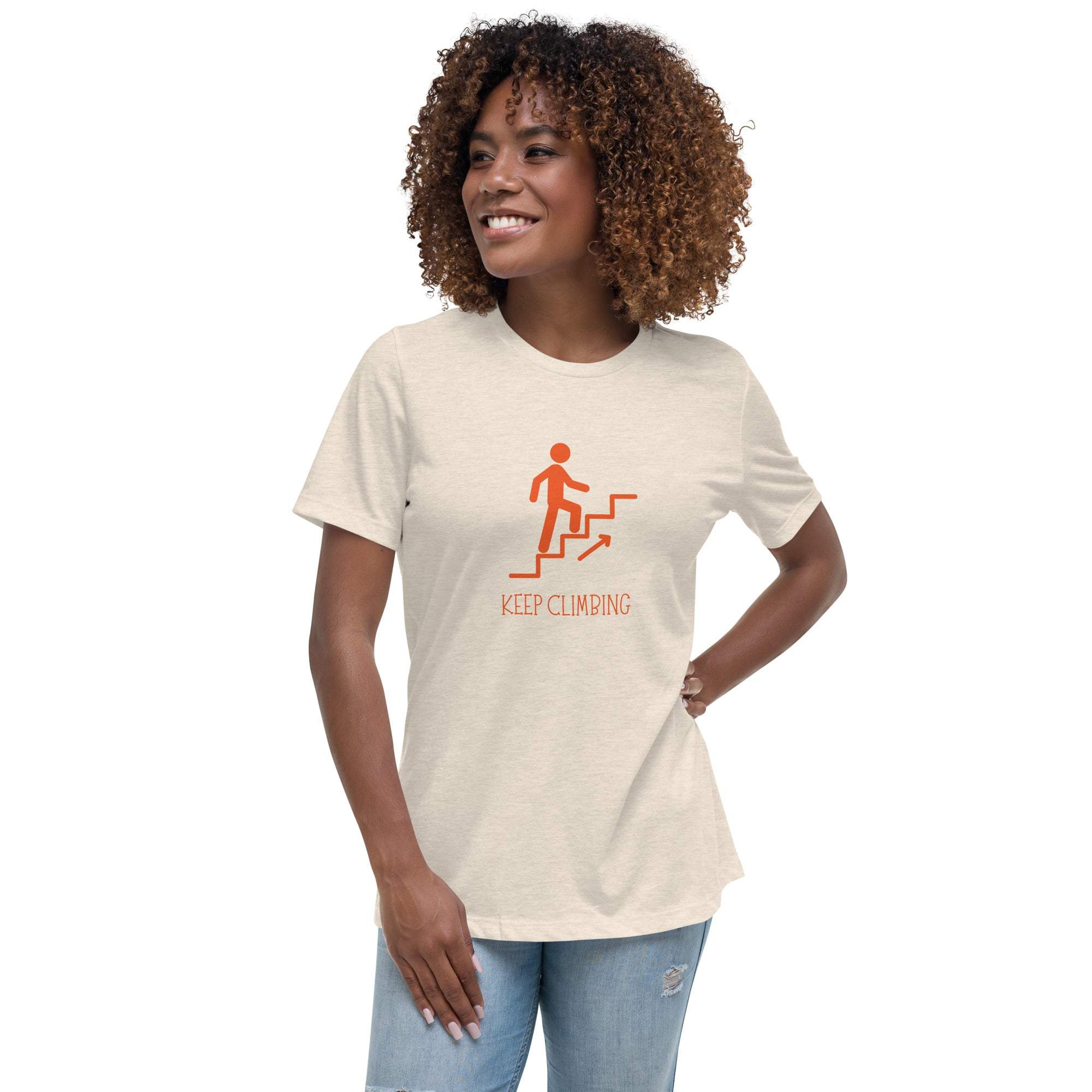 Woman wearing beige Keep Climbing women's t-shirt with motivational graphic and text, paired with light blue jeans.