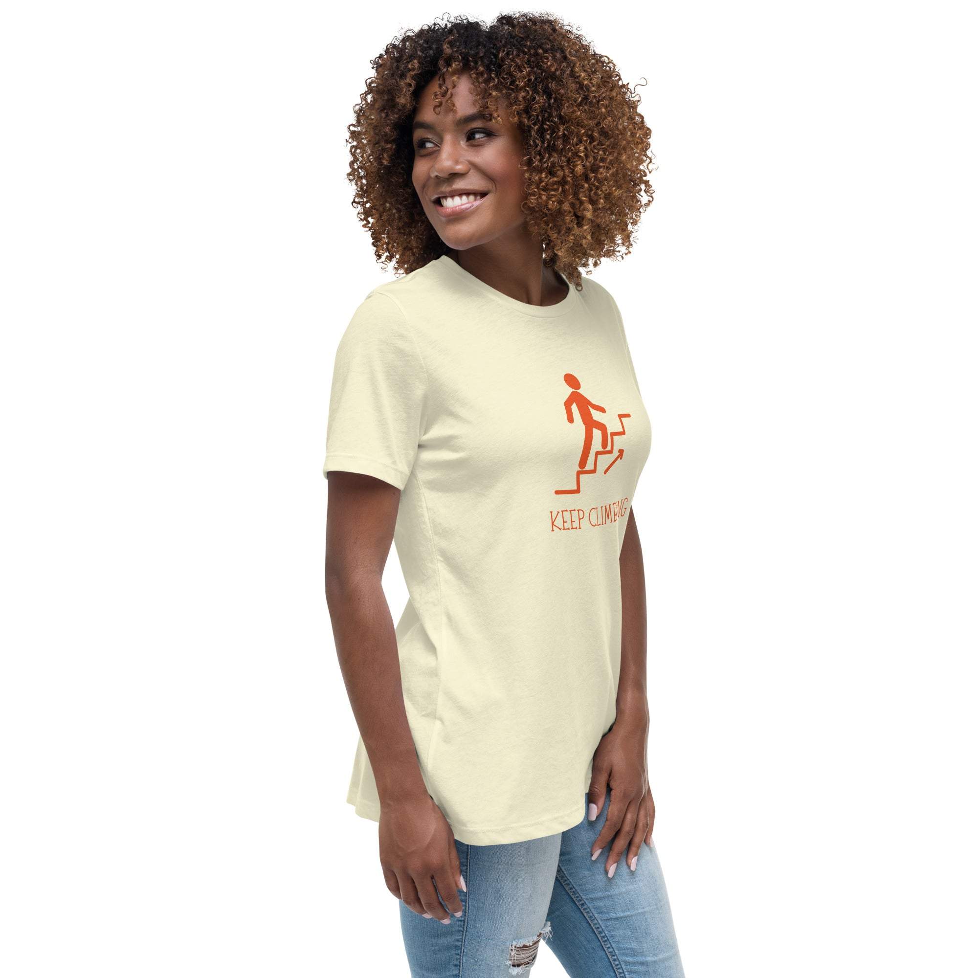 Woman wearing a beige Keep Climbing women's t-shirt with an inspirational graphic of a person climbing stairs in orange.