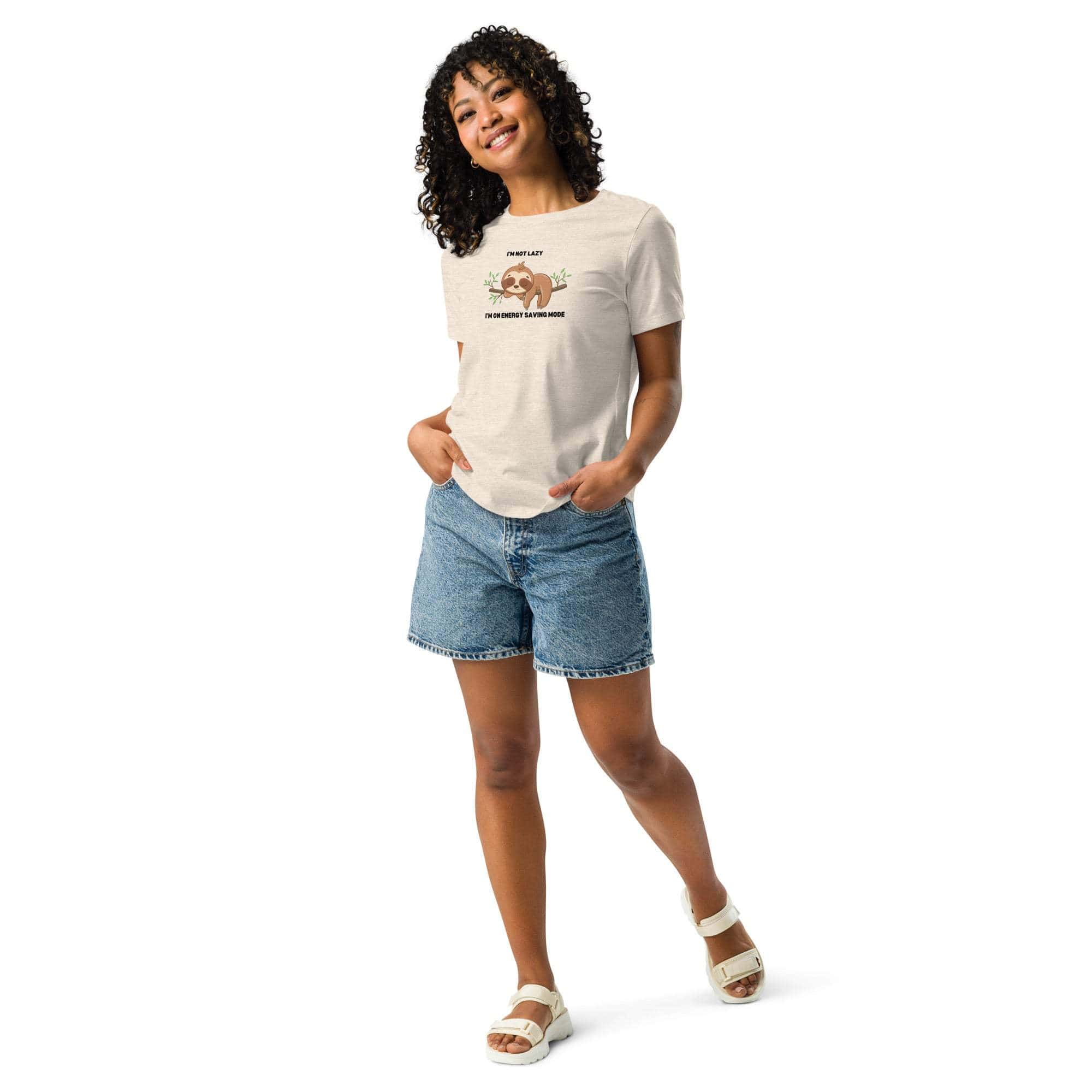 Woman wearing a beige relaxed fit T-shirt with a cute sloth graphic and "I'm Not Lazy, I am On Energy Saving Mode" caption paired with denim shorts and white sandals