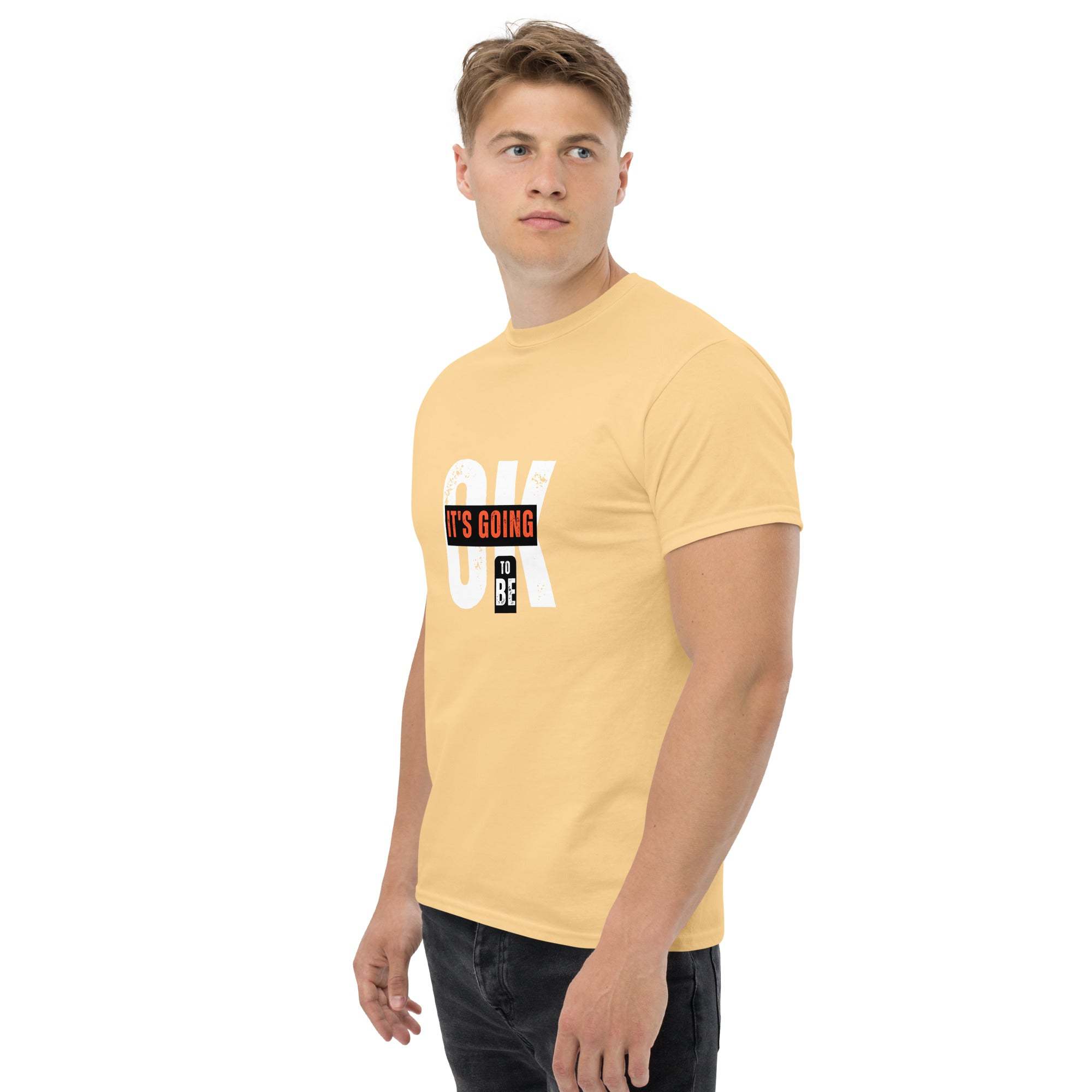Man wearing yellow trendy graphic t-shirt with motivational quote "OK it's going to be" standing against white background
